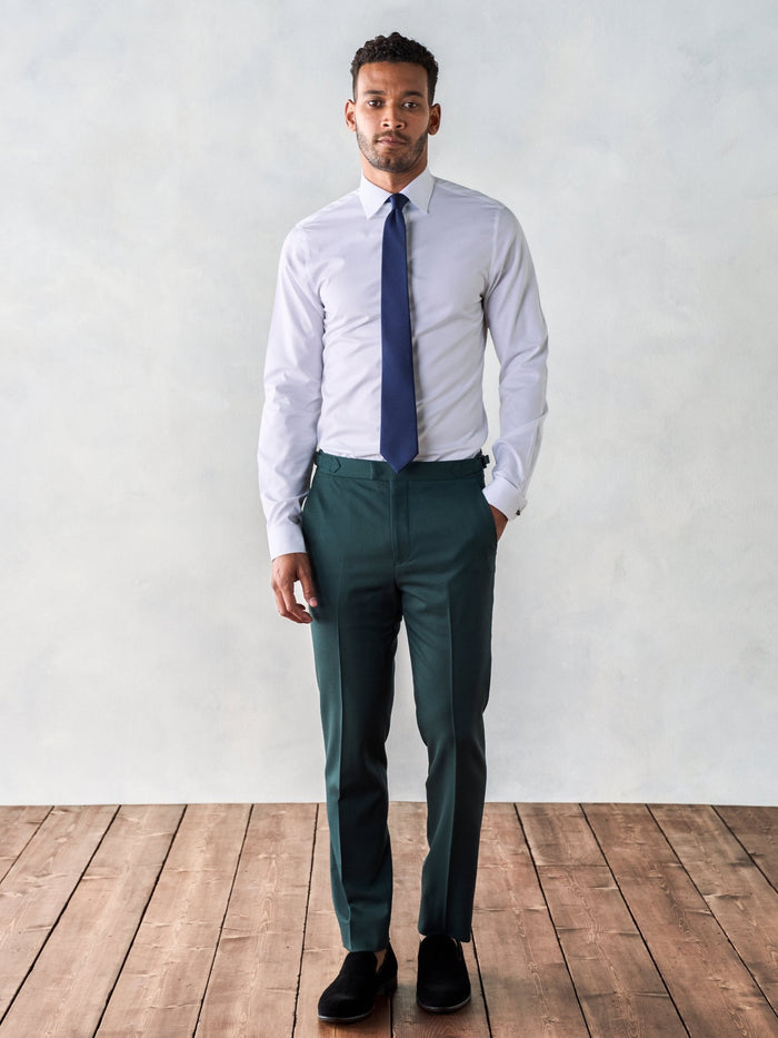 Man in a white dress shirt, navy tie, and emerald green trousers, full length.