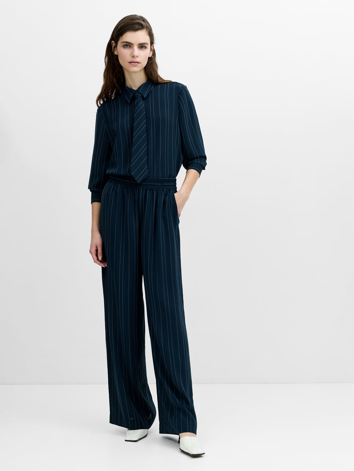 Woman wearing navy high waisted wide leg trousers with a relaxed fit and side pockets.