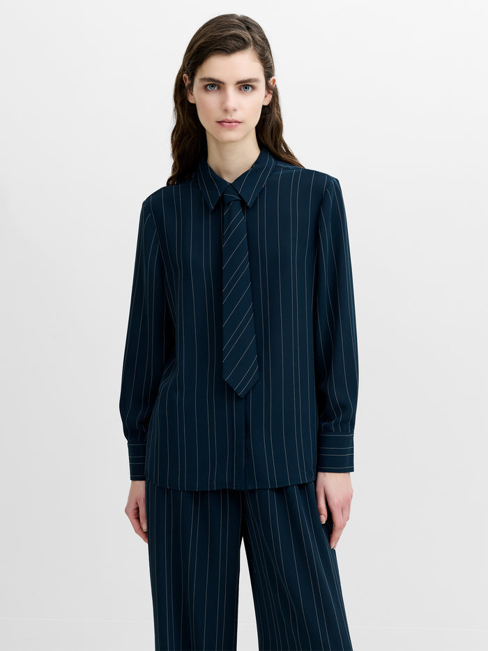 A woman wearing a relaxed fit navy pinstripe shirt with long sleeves, a shirt collar and a tie neckline.