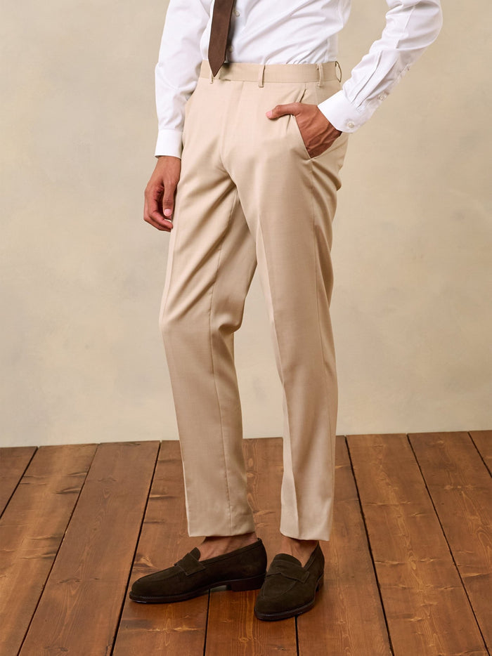 Man from waist down wearing beige trousers with a hand in the pocket, on a wood floor.