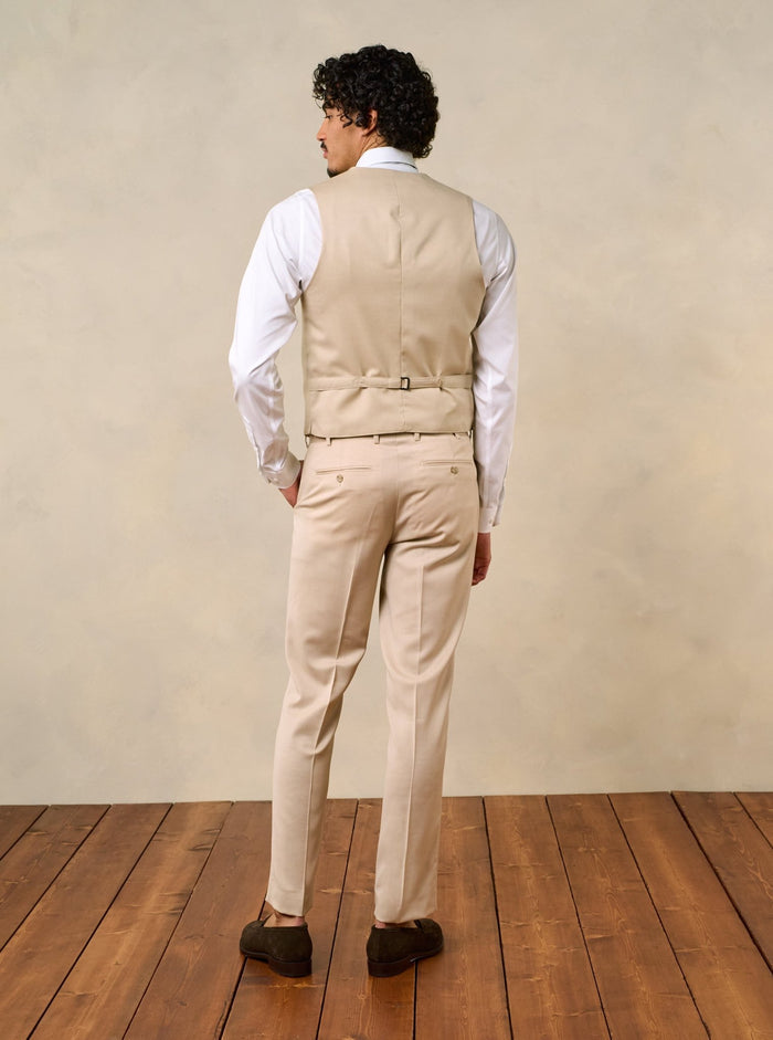 Man wearing a beige vest and pants, viewed from the back, standing on wooden floor.