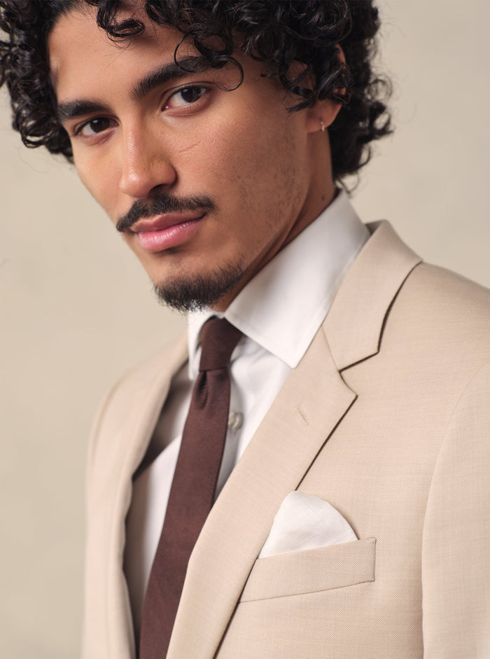 Man in a beige suit with a brown tie and white pocket square.