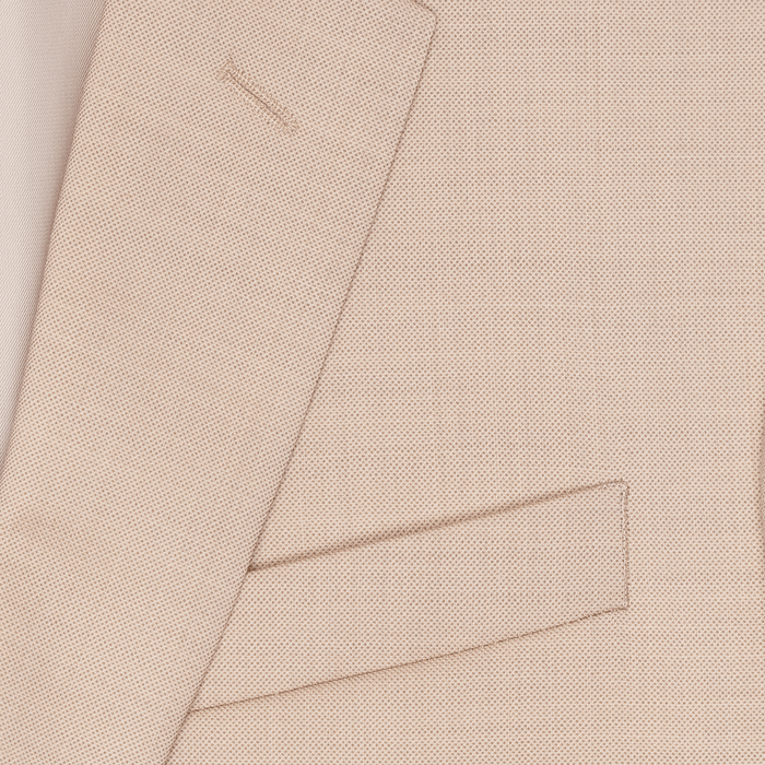 Close-up of beige suit fabric weave, showing lapel edge and flap pocket.