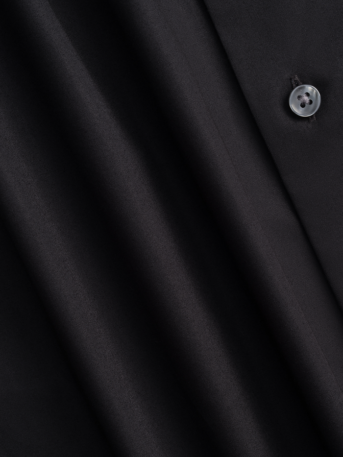 Close-up of black dress shirt fabric with folds and a button.