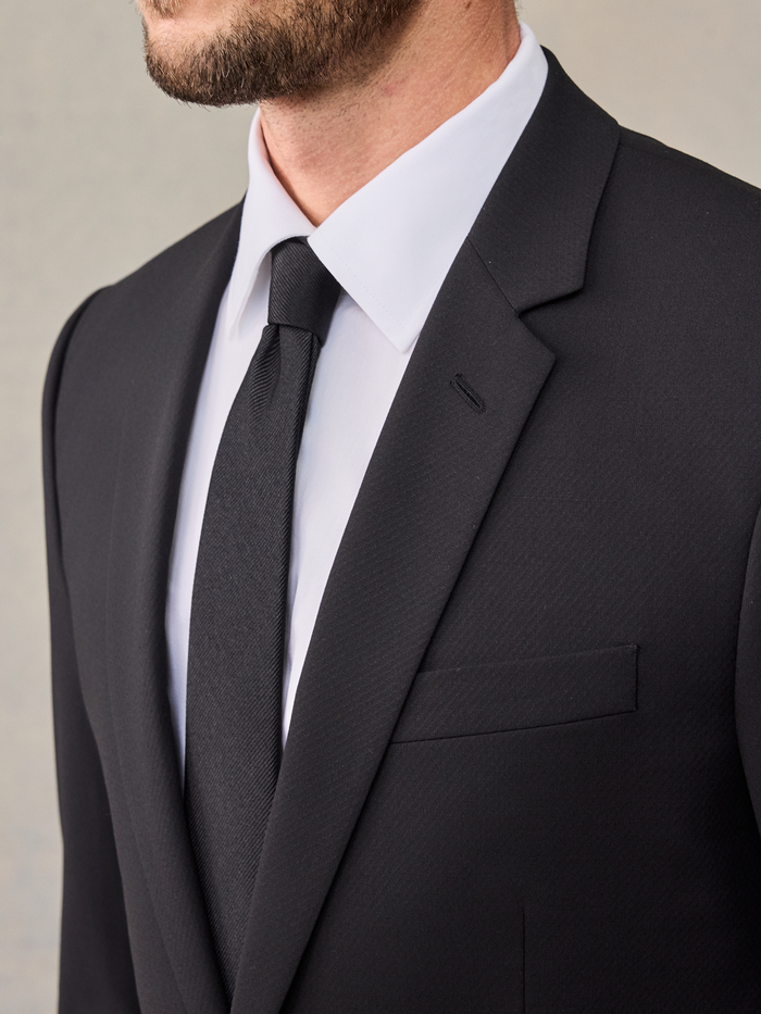Close-up of a man's black suit lapel, tie knot, and shirt collar.