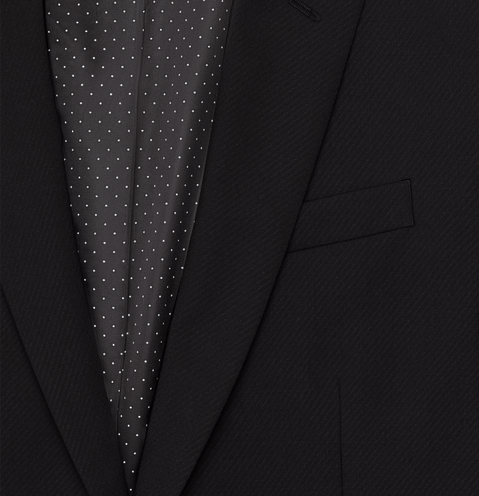 Close-up of black suit jacket lapel and welt pocket, revealing polka dot lining.