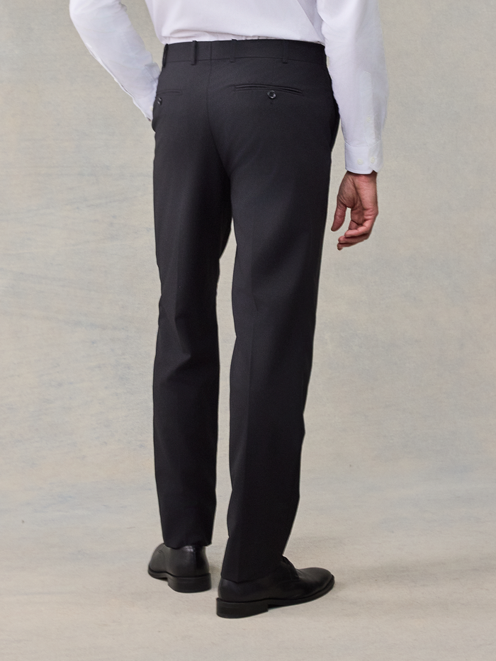 Back view of a man from waist down wearing black suit trousers.