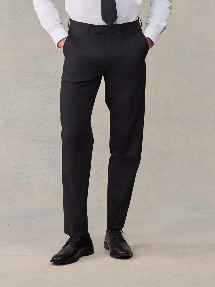 Man from waist down wearing black suit trousers, with a black tie visible above.