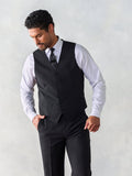 Man in a black suit vest with a patterned tie and matching trousers, looking down.
