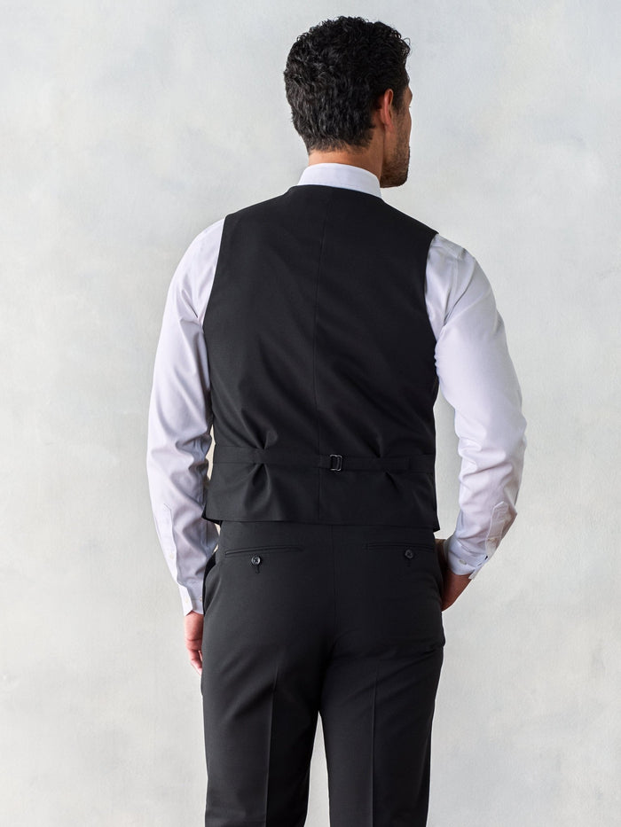 Back view of a man in a black suit vest and matching trousers.