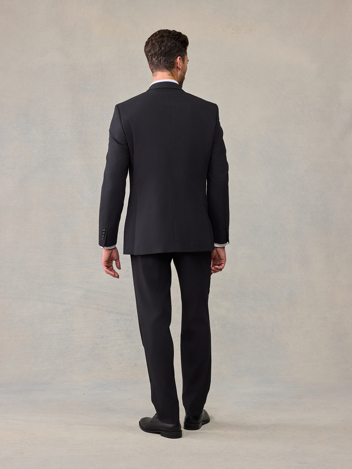 Back view of a man walking in a black suit and trousers.