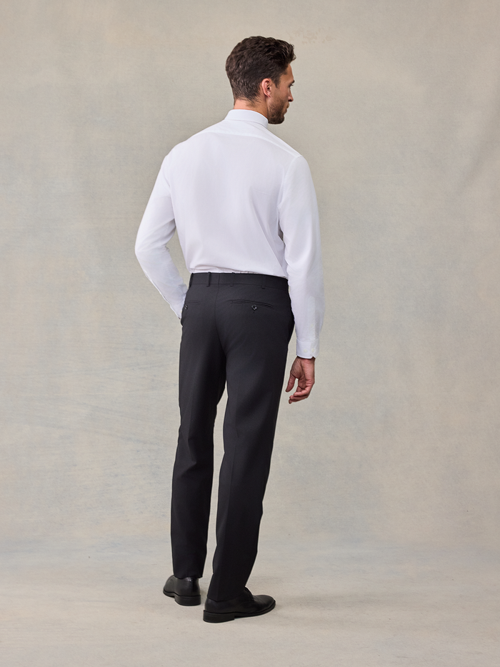 Back view of a man in a white dress shirt and black trousers, no jacket.
