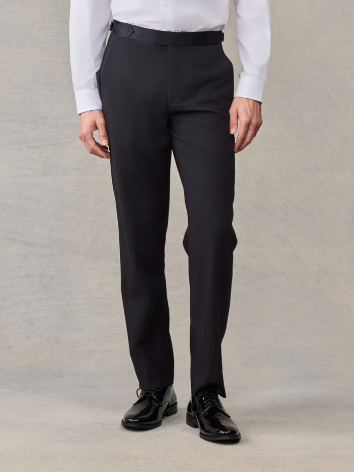 Man from waist down wearing black tuxedo trousers with a satin waistband trim.