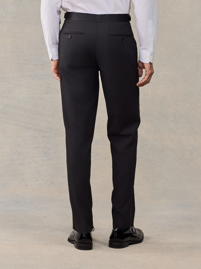 Back view of a man from waist down wearing black tuxedo trousers.