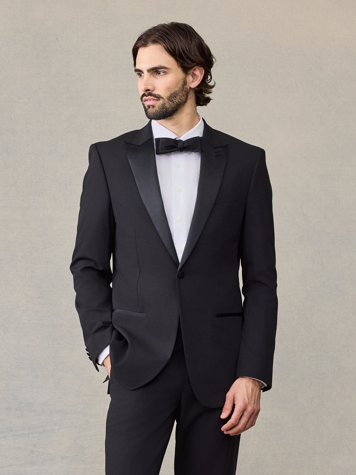 Man in a black tuxedo jacket with satin peak lapels and a black bow tie.