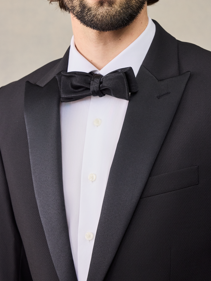 Close-up of a black bow tie and satin peak lapel on a black tuxedo jacket.