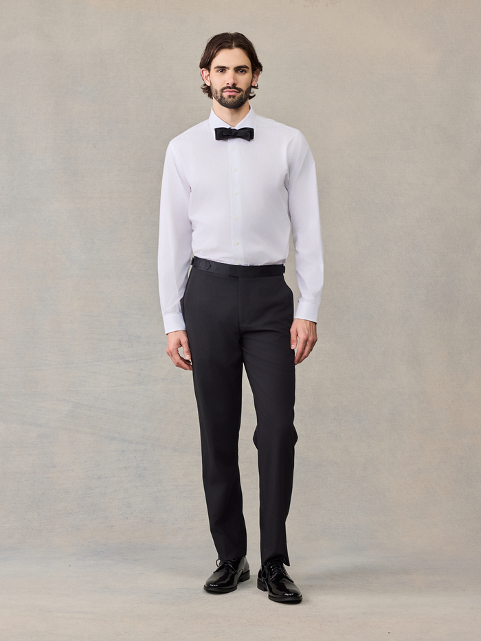 Man in a white tuxedo shirt with a black bow tie and black trousers, no jacket.
