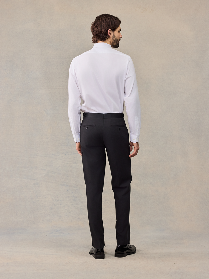 Back view of a man in a white dress shirt and black tuxedo trousers, no jacket.