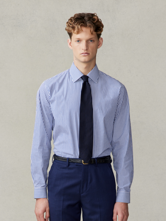 Man in a navy striped dress shirt with a navy tie and navy trousers.