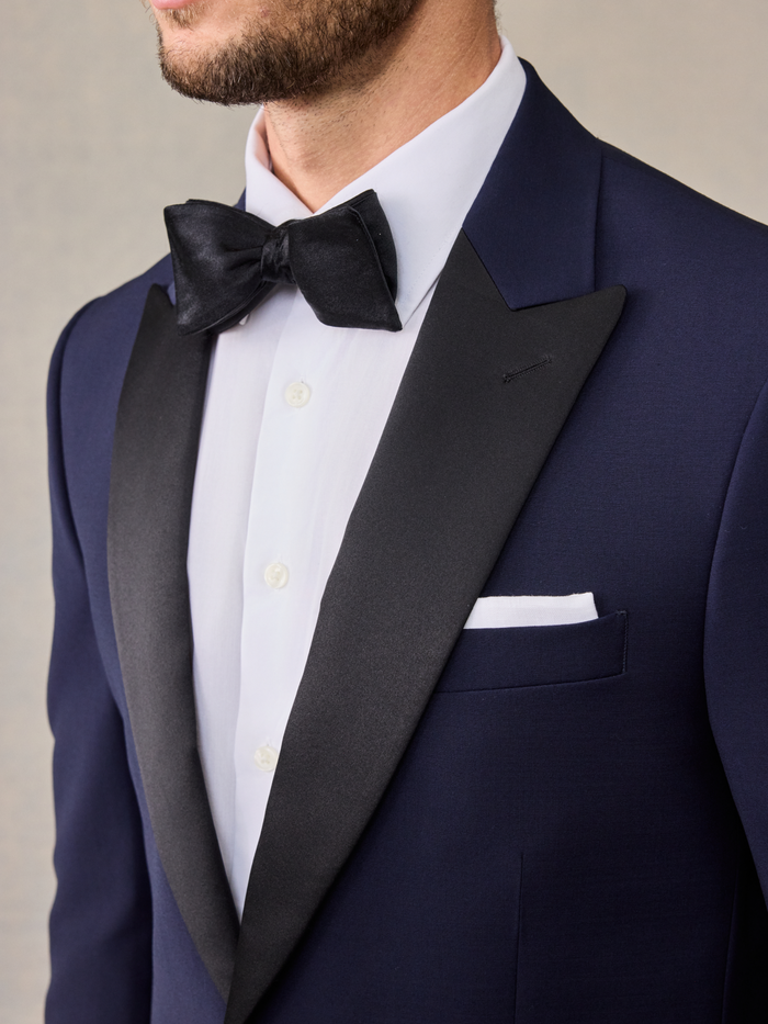 Close-up of a black bow tie and satin peak lapel on a navy tuxedo jacket.