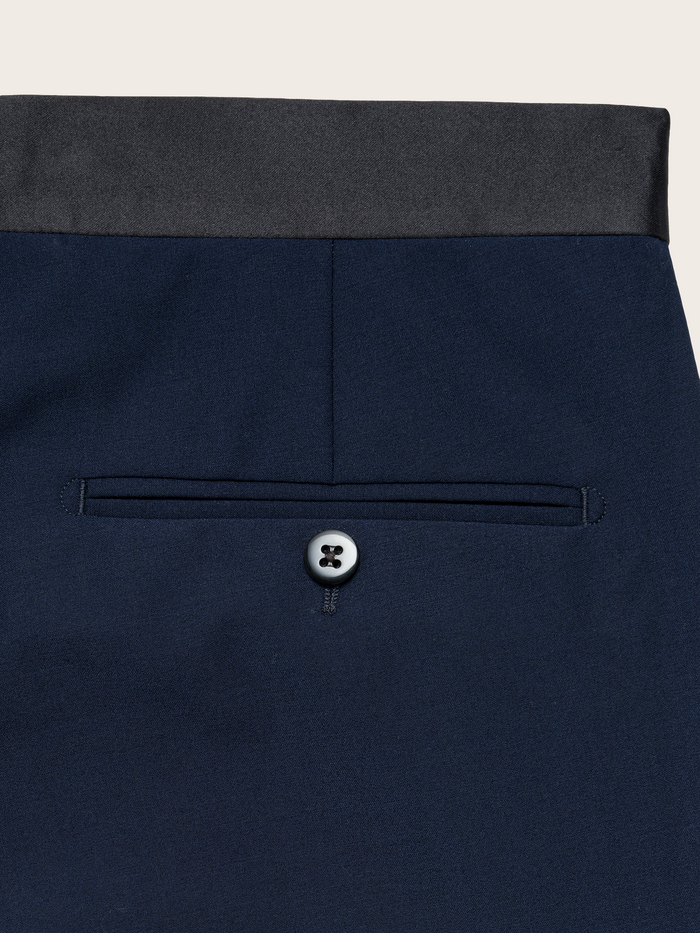 Close-up of navy tuxedo trouser back pocket with button and satin waistband.