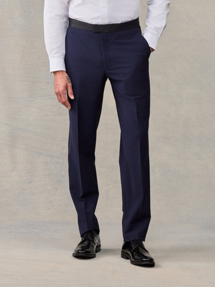 Man from waist down wearing navy tuxedo trousers with a satin waistband.