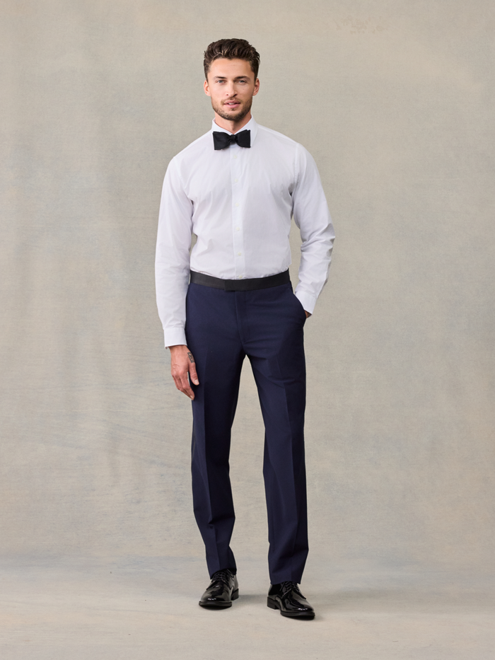 Man in a white tuxedo shirt with a black bow tie and navy trousers, no jacket.