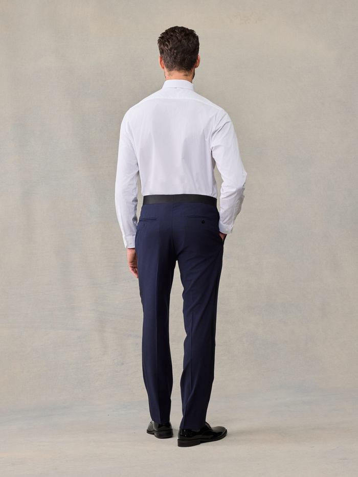 Back view of a man in a white tuxedo shirt and navy trousers, no jacket.