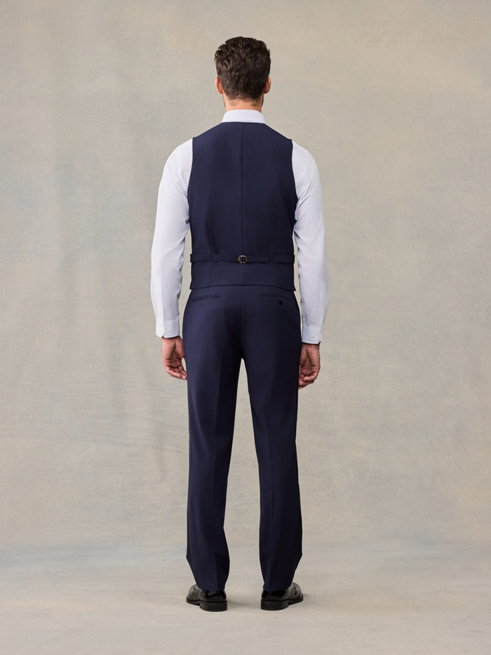 Back view of a man in a navy tuxedo vest and trousers, full length.