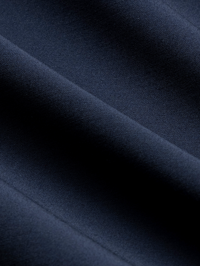 Close-up of navy tuxedo fabric with folds, showing a subtle diagonal seam.