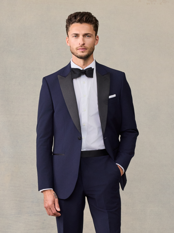 Man in a navy tuxedo jacket with black satin peak lapels and a black bow tie.