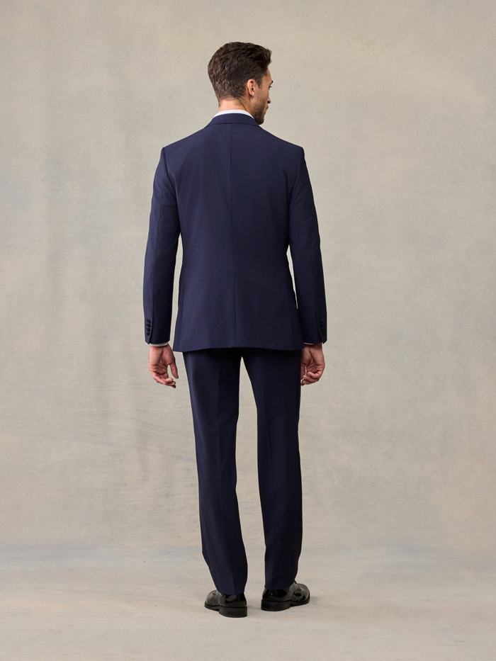 Back view of a man in a navy tuxedo jacket and trousers, full length.