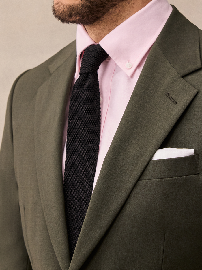 Close-up of an olive suit lapel, black knit tie, and white pocket square.