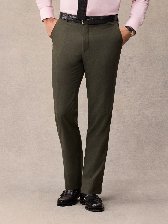 Man from waist down wearing olive suit trousers with a black belt, hands in pockets.