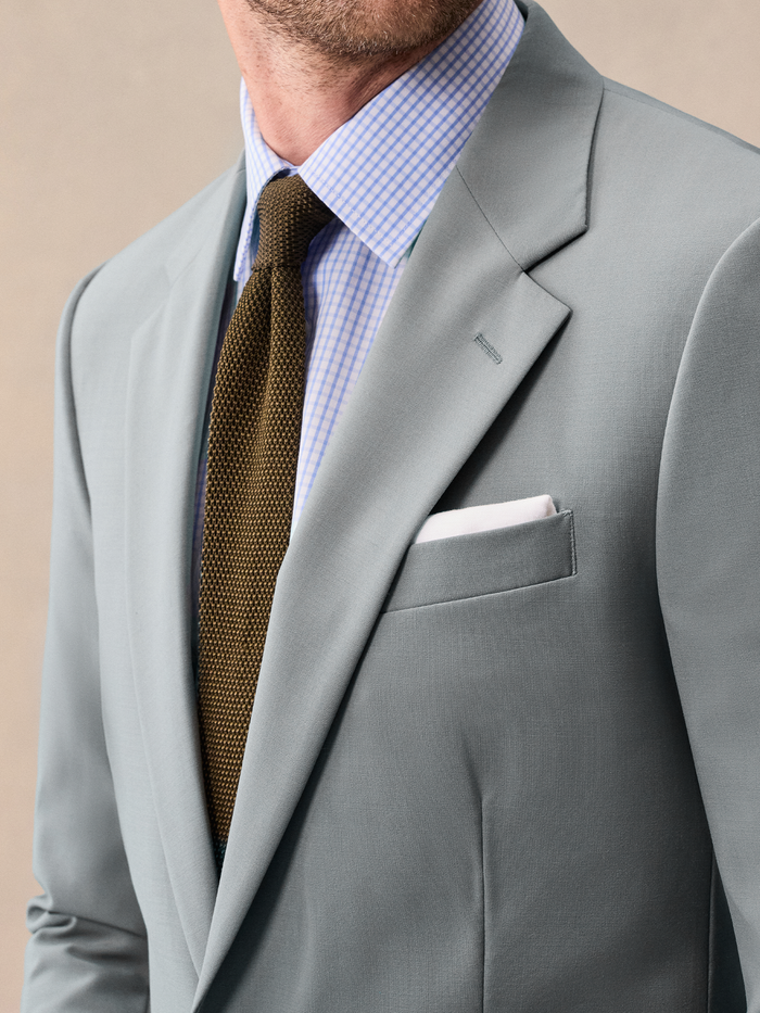 Close-up of a sage suit lapel, olive knit tie, and white pocket square.