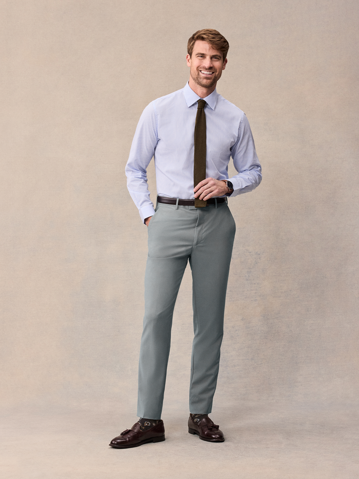 A man in a striped shirt and olive tie with sage suit trousers and brown belt