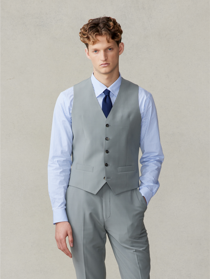 Man in a sage suit vest with a striped shirt and navy tie.