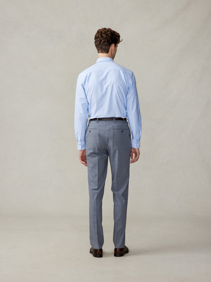 Man in a light blue shirt and slate grey suit trousers, viewed from the back.