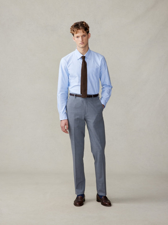 Man in a light blue shirt and brown tie with slate grey trousers, no jacket.