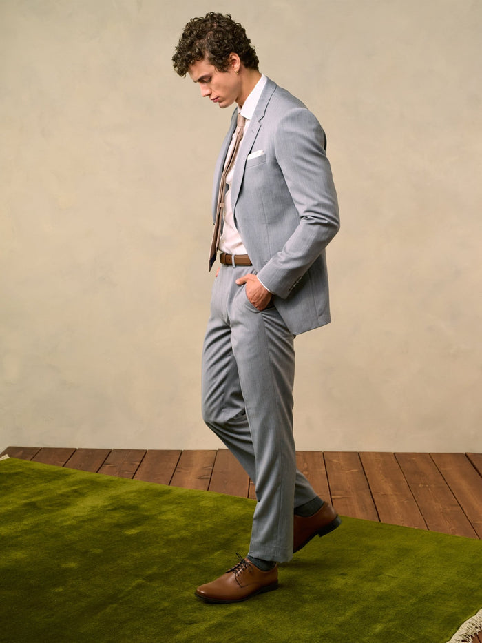 Side profile of a man in a sterling grey three-piece suit, looking down.