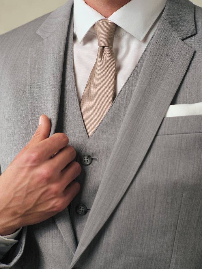 Close-up of a sterling grey suit vest, tan tie, and white pocket square.