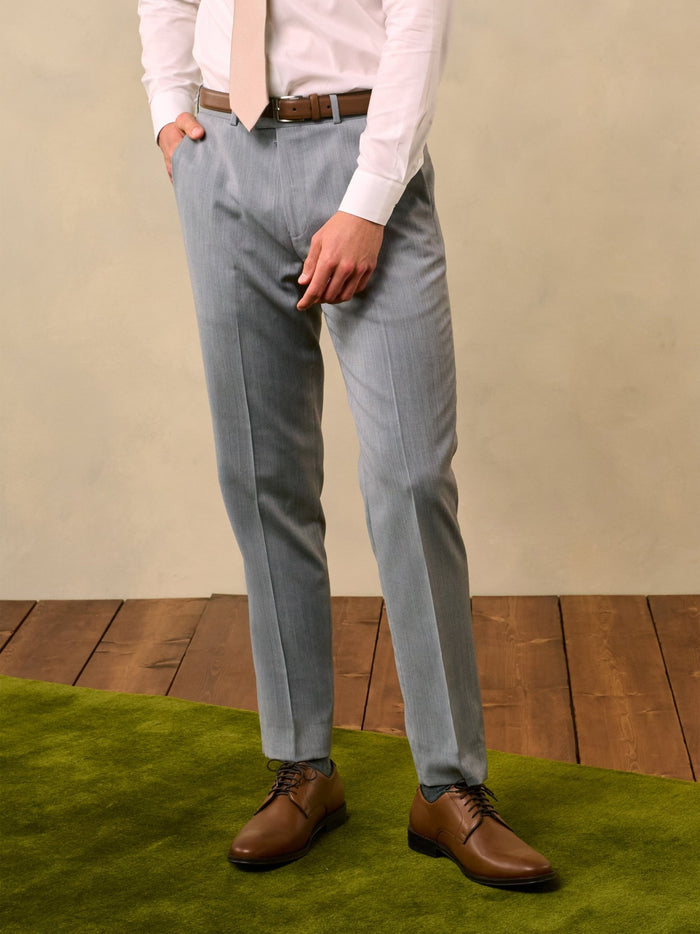Man from waist down wearing sterling grey trousers with a tan belt.