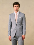 A man in a sterling grey suit with blue shirt and brown knit tie, side profile