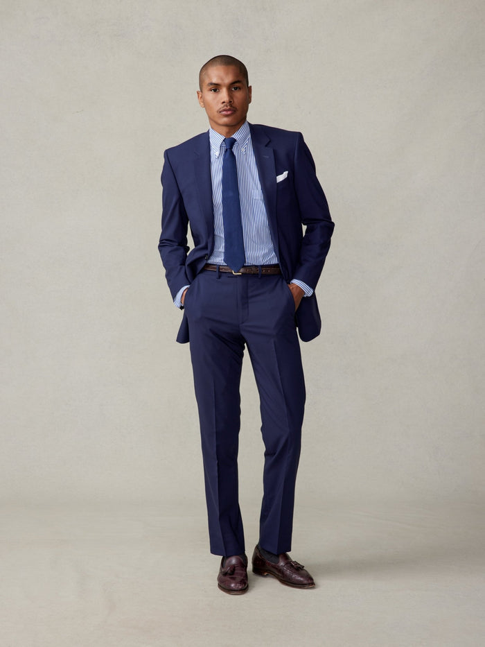 Man in a true navy suit with a striped shirt and navy tie against a neutral background.