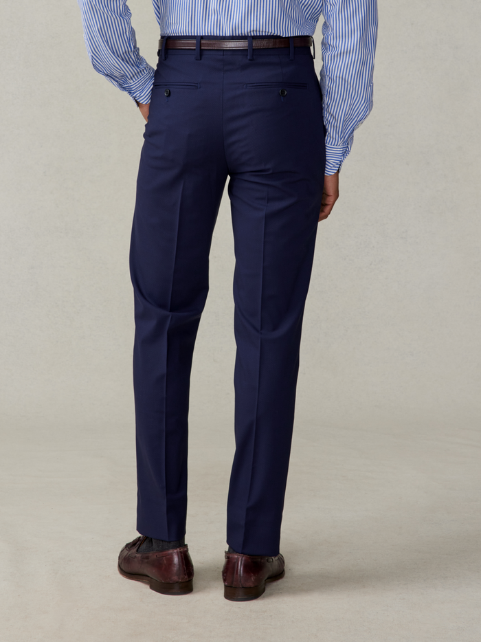 Back view of a man from waist down in true navy suit trousers and brown loafers.
