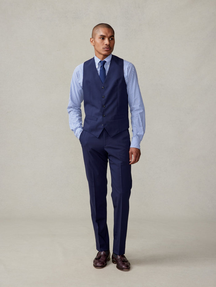 Man walking in a true navy suit vest with a striped shirt and navy tie.