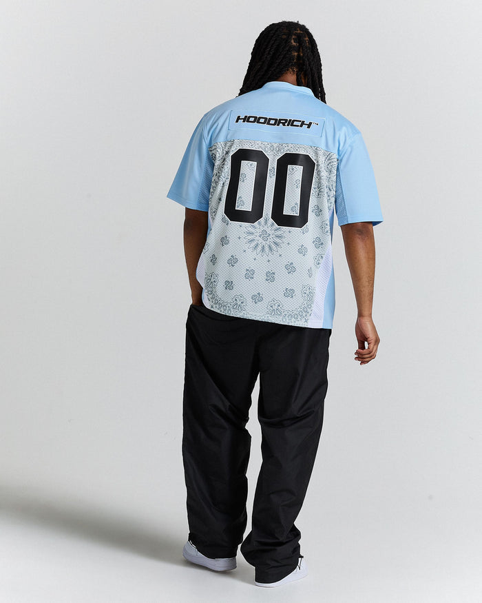 Person wearing a light blue shirt with 'HOODRICH' branding and black pants on a white background
