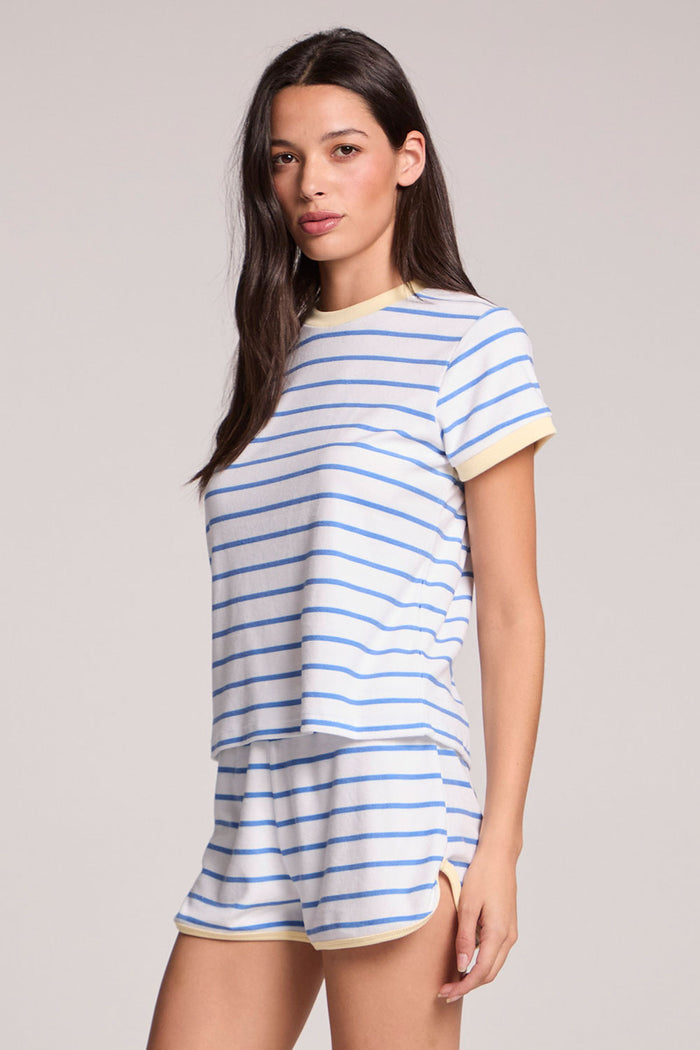 Side angle view of a woman wearing the Chaser  Evalina Blue Hydrangea Stripe Tee on a neutral background with arms at her side