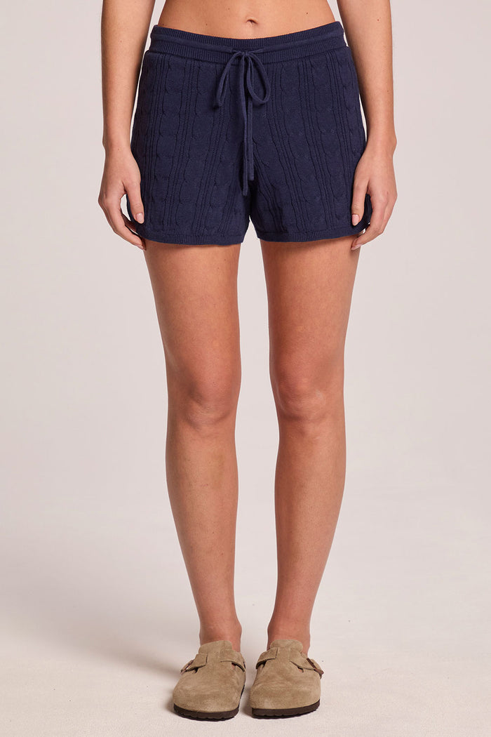 A front view of a woman wearing the Chaser Evie Admiral Shorts and clogs on a neutral background