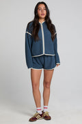A full body front view of a woman wearing the Chaser  Eyla Dark Denim Shorts on a neutral background